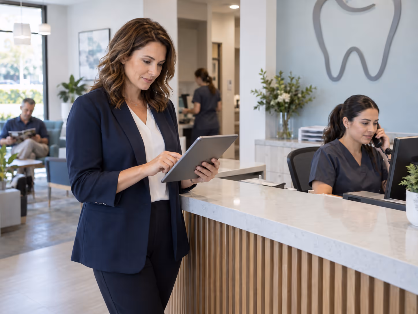 A dental practice manager reviews digital inquiries on a tablet while the front desk handles a call.